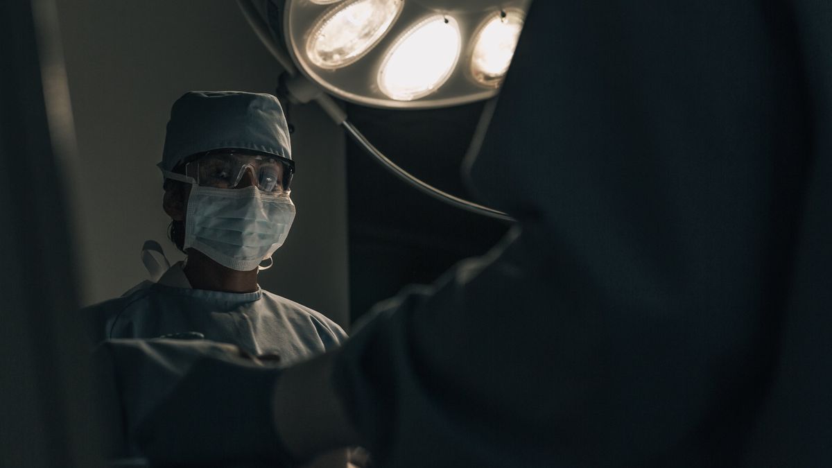 Cirujano con cubrebocas bajo la lámpara de un quirófano