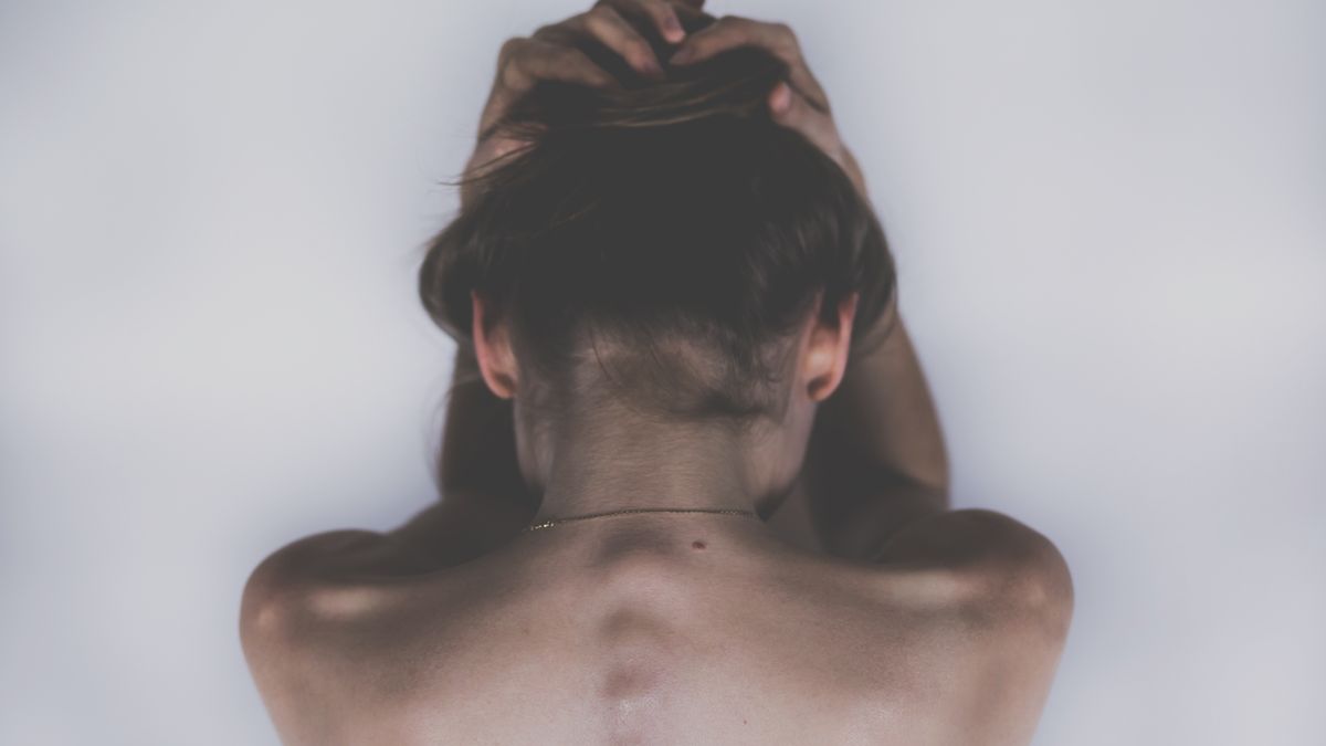 Mujer de espaldas con las manos en la nuca por dolor de cuello y espalda